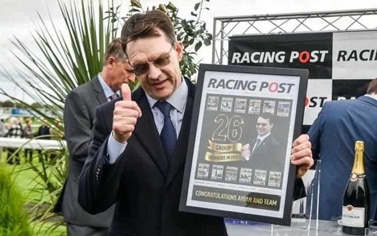 Trainer Aidan O’Brien holding a picture frame with a Racing Post newspaper inside.