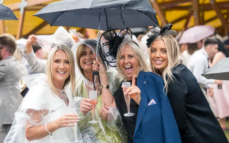 A group of race goers in rain macs holding champagne at Doncaster