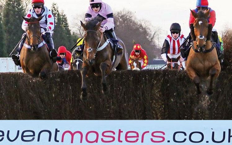 Jockeys on horses jumping over a hurdle.