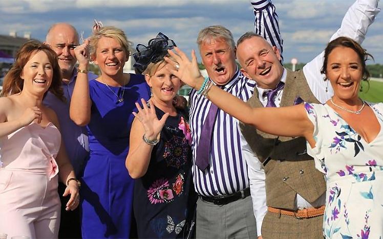 A group of people dressed for the races pose for a photo