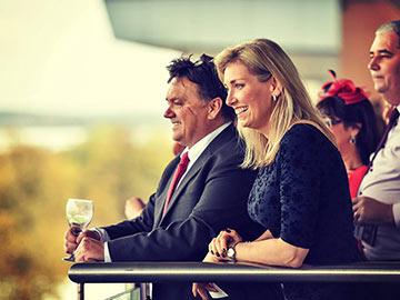 A man and Woman enjoy a glass of wine while watching the race from their balcony