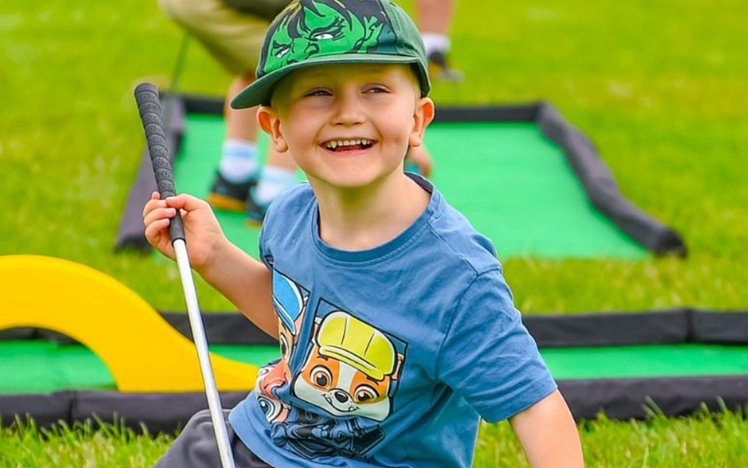 Child smiling holding a golf putter