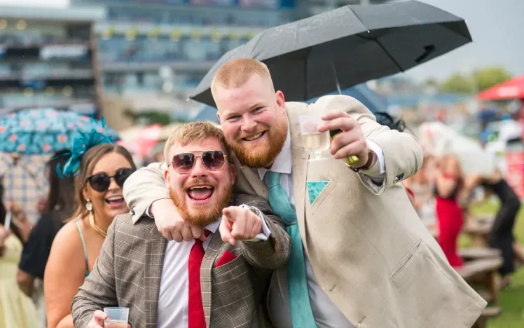 Two race goers in suits at Doncaster point to the camera