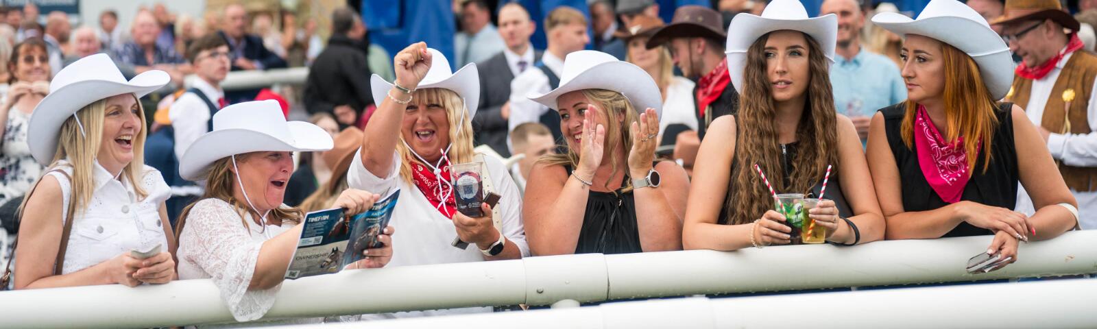 A group of racegoers dressed as cowgirls line the track at Doncaster with one holding a race card